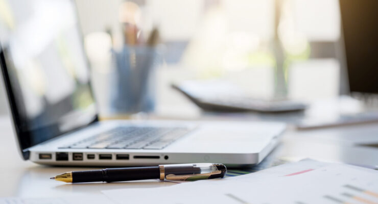 Laptop und Stift mit Papieren auf einem Schreibtisch